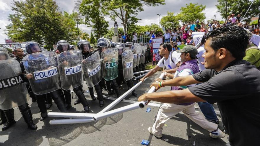 Gente revolotean banderas nacionales nicaragüenses frente a una línea de policías antidisturbios que protestan contra el sistema electoral en Managua , Nicaragua.
