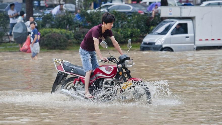Vehículos y residentes hacen su camino a través de una calle inundada en Wenling, en la provincia oriental china de Zhejiang, el 10 de agosto 2015, después que fuertes tormentas golpearon el área durante la recalada del tifón Soudelor.