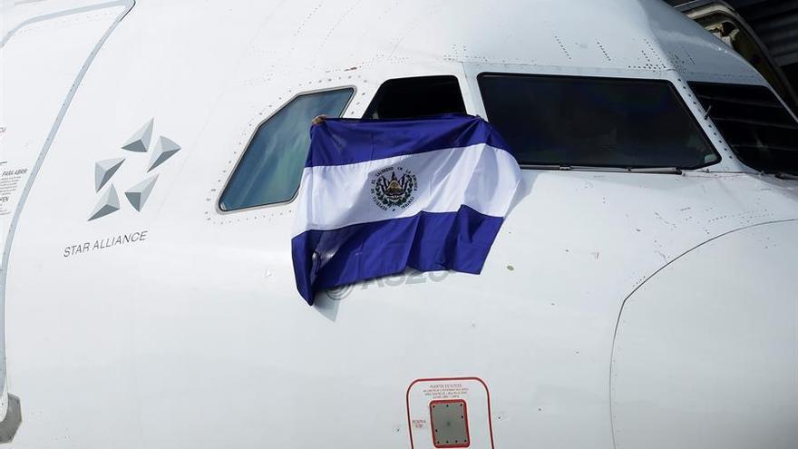 Miembros de la tripulación de un vuelo comercial muestran hoy la bandera salvadoreña en el Aeropuerto Internacional San Óscar Arnulfo Romero y Galdámez.