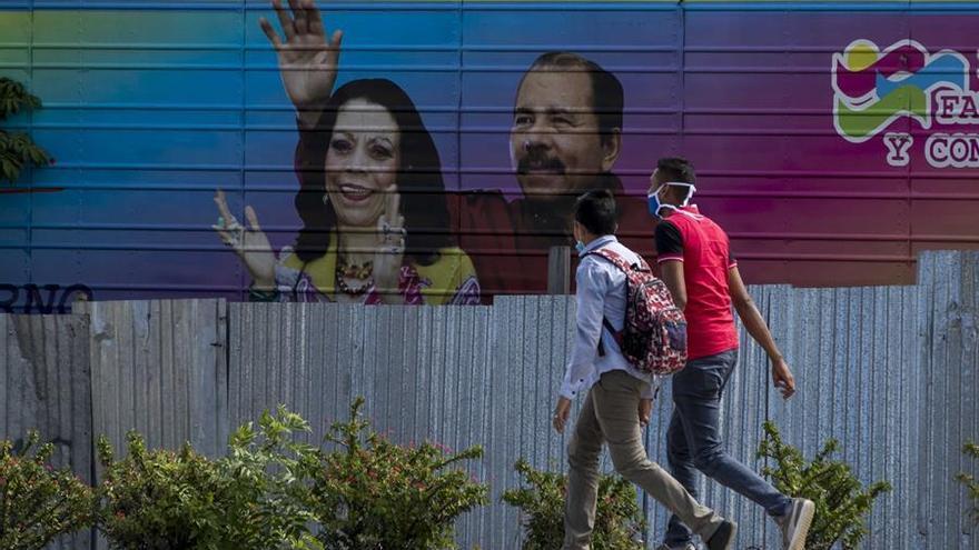 Dos jóvenes fueron registrados al caminar frente una pancarta con la imagen del presidente de Nicaragua, Daniel Ortega (d), y su esposa, Rosario Murillo (i), en Managua (Nicaragua).