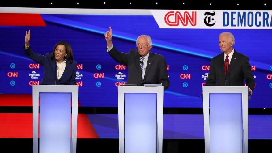 La senadora Kamala Harris (i) y el senador Bernie Sanders (c) levantan sus manos, mientras el ex-vicepresidente Joe Biden mira durante el pasado debate presidencial del partido Demócrata.