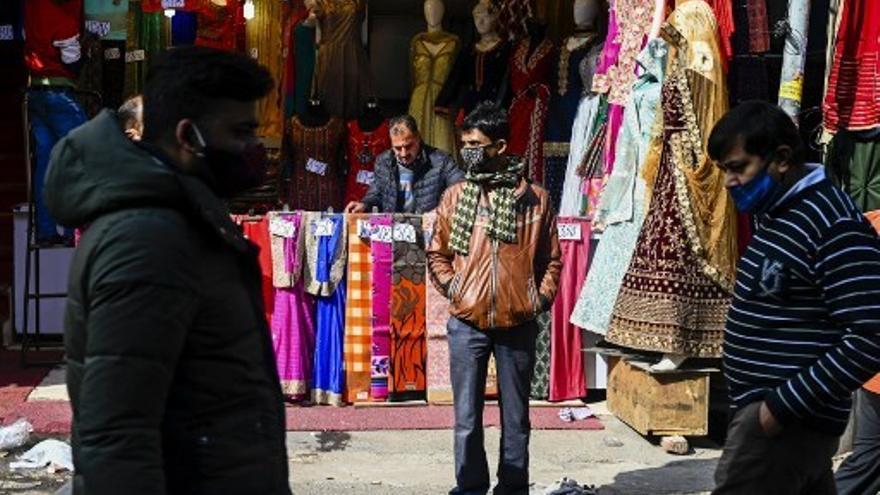 Personas caminan en India frente a locales de ventas de ropas y telas