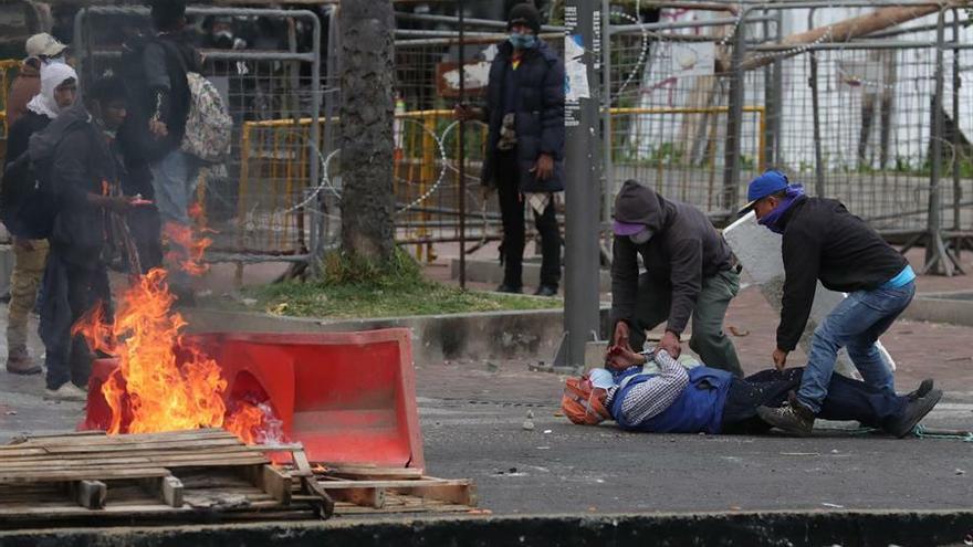 Dos hombres ayudan a un herido mientras la policía y manifestantes se enfrentan durante una nueva jornada de protestas con presencia indígena este viernes, en Quito (Ecuador).